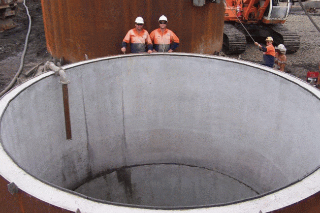 Two men standing at top of blind bored mine ventilation shaft